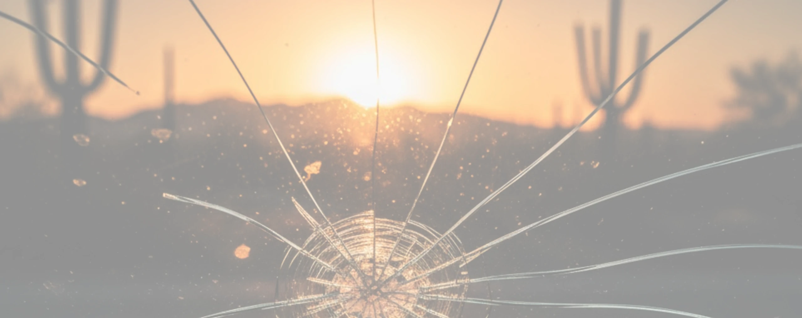 Cracked windshield with a rock chip spreading from Tucson heat; Saguaro desert background.